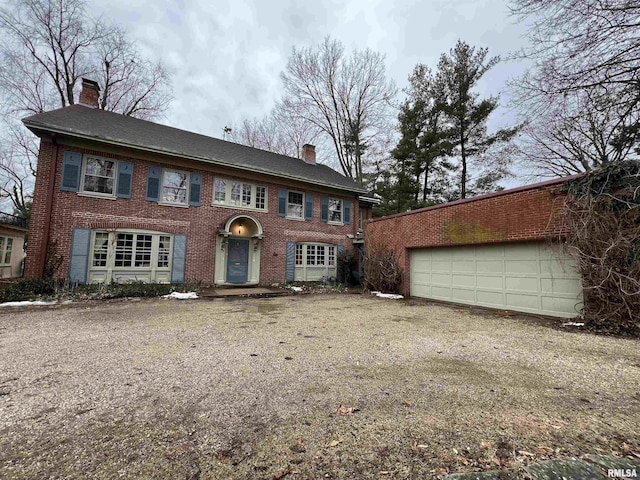 view of front of home with a garage, brick siding, and a chimney