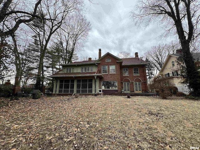 rear view of house featuring brick siding, a chimney, and a sunroom