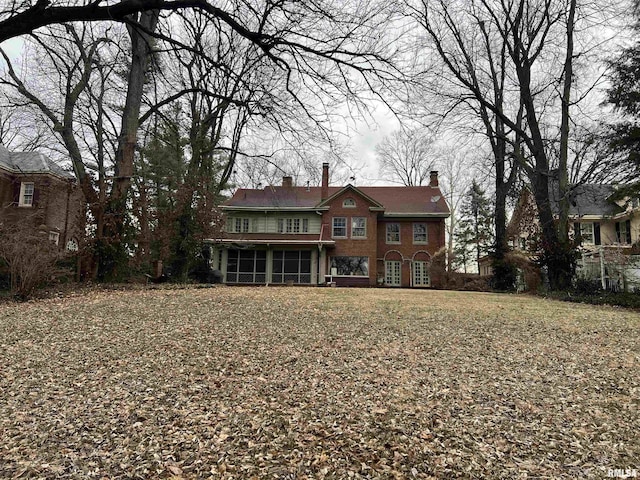 back of house featuring brick siding, a chimney, and a sunroom