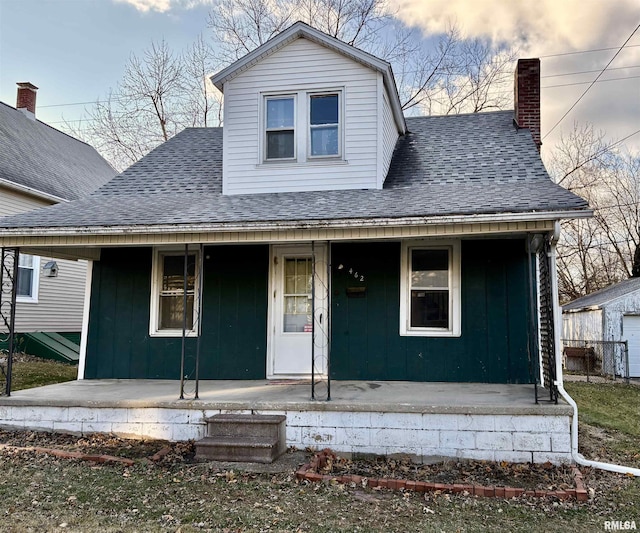 view of front of house with a porch, roof with shingles, a chimney, and board and batten siding