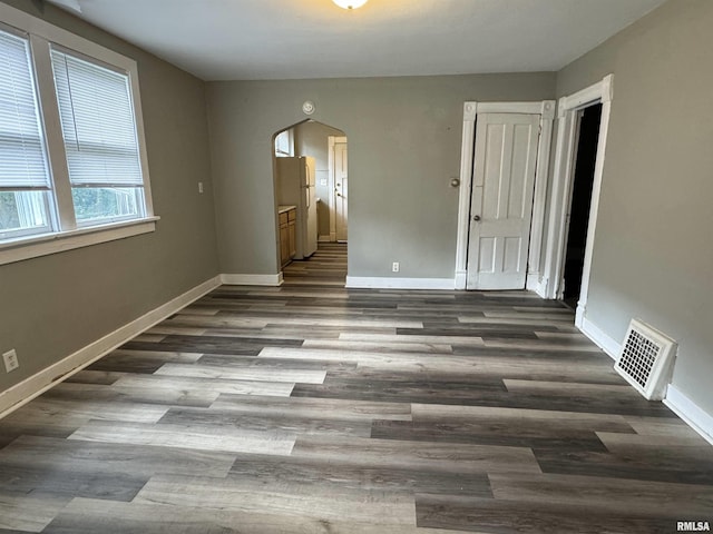 empty room featuring baseboards, visible vents, arched walkways, and dark wood finished floors