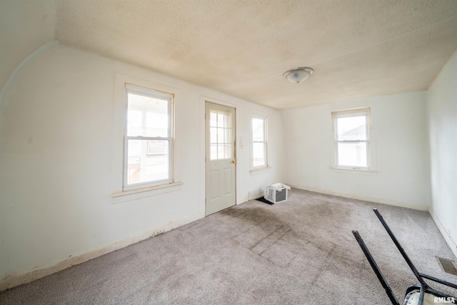 empty room featuring light carpet, vaulted ceiling, and a textured ceiling