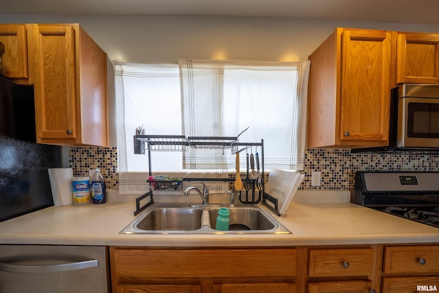 kitchen with appliances with stainless steel finishes, light countertops, a sink, and decorative backsplash