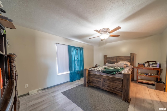 bedroom featuring a textured ceiling, visible vents, baseboards, a ceiling fan, and light wood-type flooring