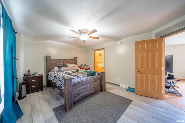 bedroom featuring a textured ceiling, light wood-style flooring, visible vents, baseboards, and a ceiling fan