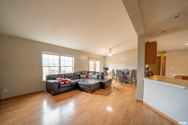 living room with baseboards, vaulted ceiling, a ceiling fan, and light wood-style floors