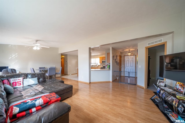 living area featuring light wood finished floors, baseboards, visible vents, and a ceiling fan