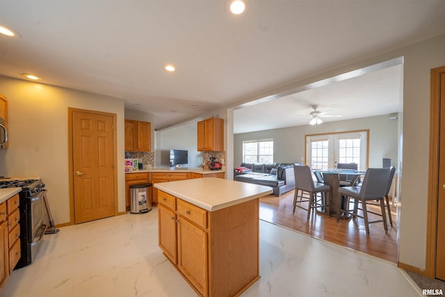 kitchen featuring marble finish floor, light countertops, a center island, tasteful backsplash, and gas stove