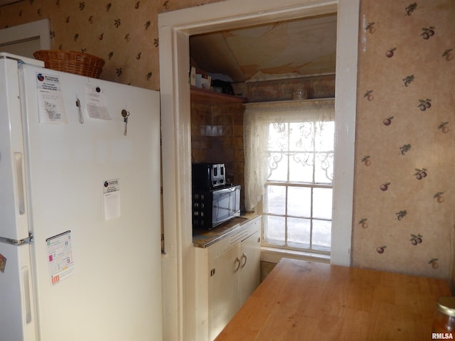 kitchen featuring butcher block countertops, freestanding refrigerator, and wallpapered walls