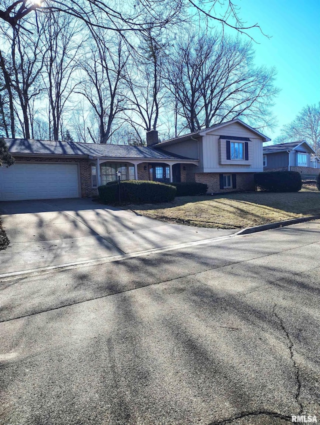 split level home featuring brick siding, a chimney, concrete driveway, an attached garage, and a front yard