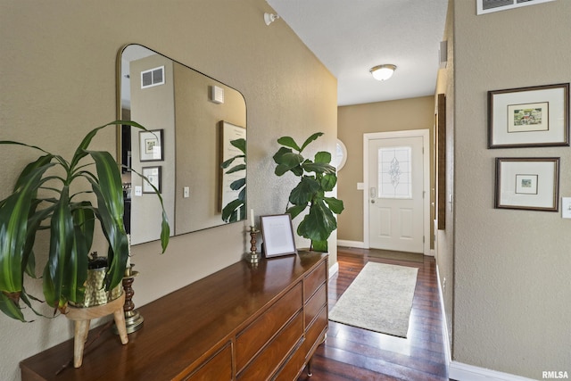 foyer featuring baseboards, visible vents, dark wood-type flooring, and a textured wall