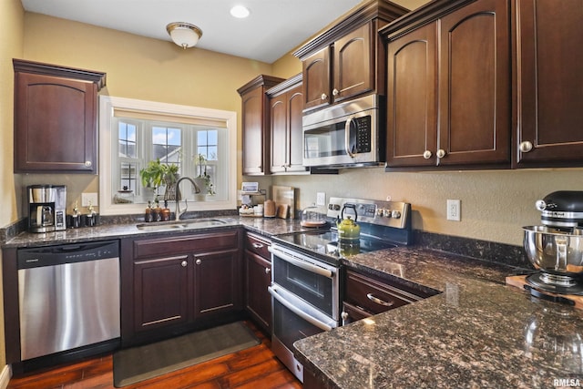 kitchen featuring dark brown cabinetry, dark stone countertops, appliances with stainless steel finishes, and a sink