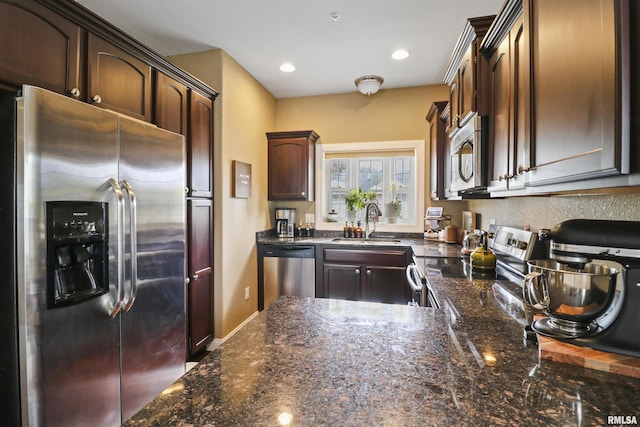 kitchen featuring recessed lighting, appliances with stainless steel finishes, dark brown cabinetry, a sink, and dark stone countertops