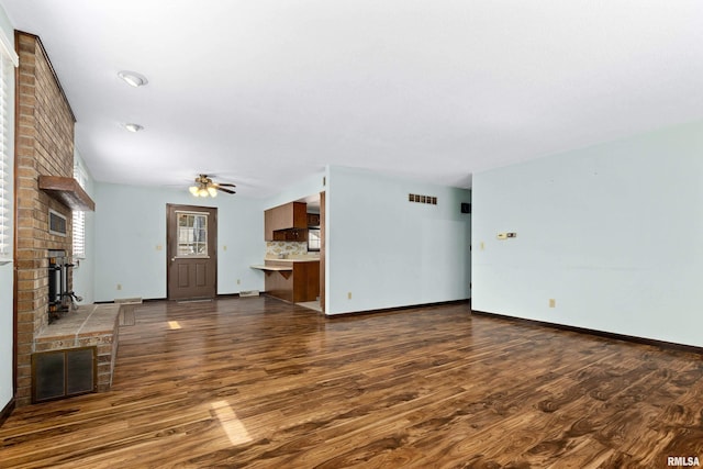 unfurnished living room with a brick fireplace, baseboards, visible vents, and wood finished floors