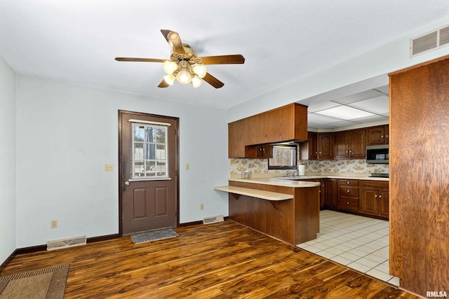 kitchen with visible vents, stainless steel microwave, a peninsula, light countertops, and light wood-type flooring