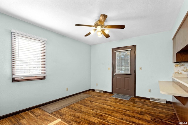 spare room with dark wood-type flooring, visible vents, ceiling fan, and baseboards