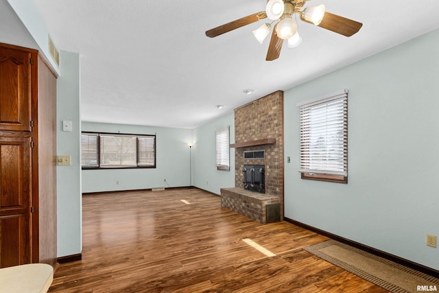 unfurnished living room featuring baseboards, visible vents, ceiling fan, wood finished floors, and a brick fireplace