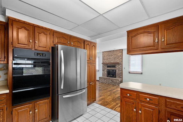 kitchen featuring oven, brown cabinetry, light countertops, and freestanding refrigerator