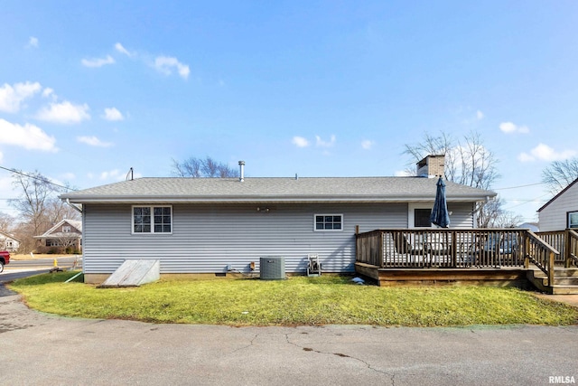 rear view of house with a chimney, roof with shingles, a deck, cooling unit, and a yard