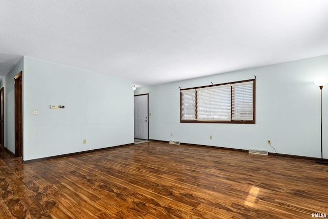 empty room with dark wood-style flooring, visible vents, and baseboards