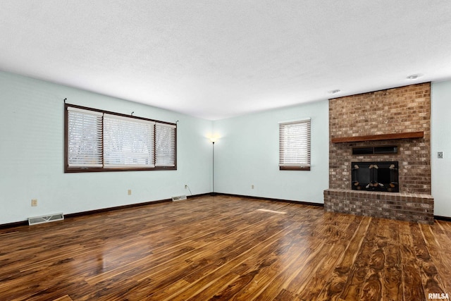 unfurnished living room with a textured ceiling, a brick fireplace, wood finished floors, and visible vents