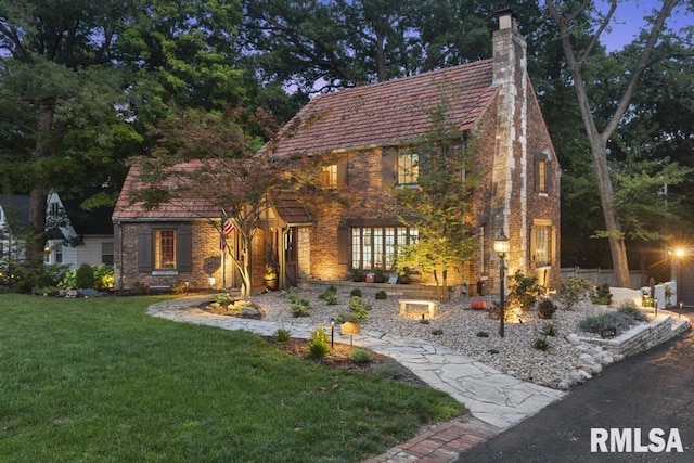 tudor-style house featuring brick siding, a chimney, and a front yard