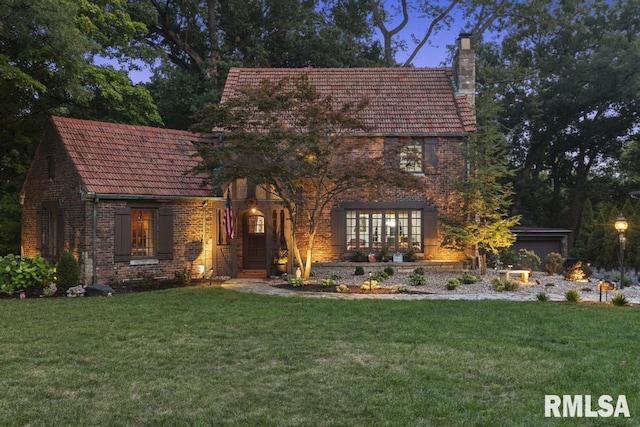 tudor-style house with brick siding, a chimney, a front lawn, and a tiled roof