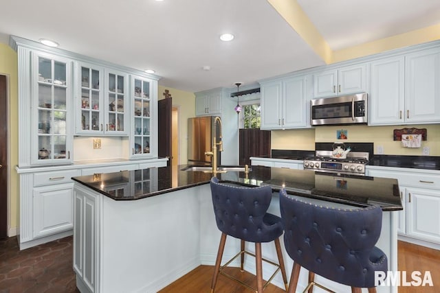 kitchen with a kitchen island with sink, a sink, white cabinets, appliances with stainless steel finishes, and glass insert cabinets