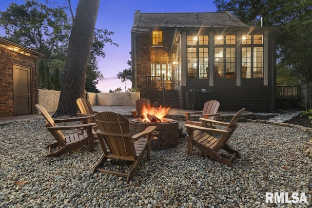 back of property at dusk with an outdoor fire pit, fence, and a patio