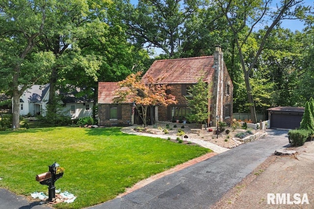 view of front of home featuring a detached garage, an outdoor structure, a chimney, and a front lawn