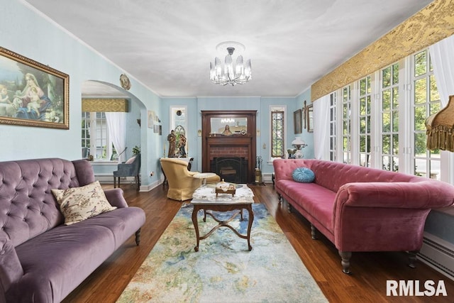 interior space with arched walkways, a brick fireplace, baseboard heating, and wood finished floors