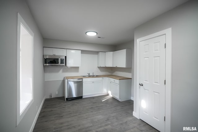 kitchen featuring dark wood finished floors, wood counters, appliances with stainless steel finishes, white cabinetry, and a sink