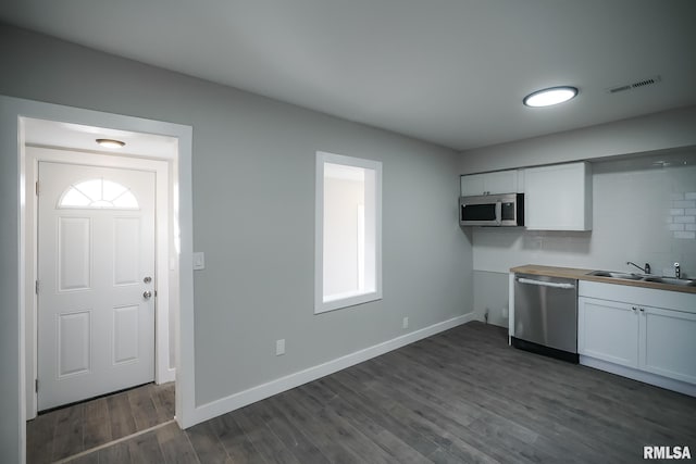 kitchen with dark wood-style flooring, appliances with stainless steel finishes, white cabinetry, a sink, and baseboards