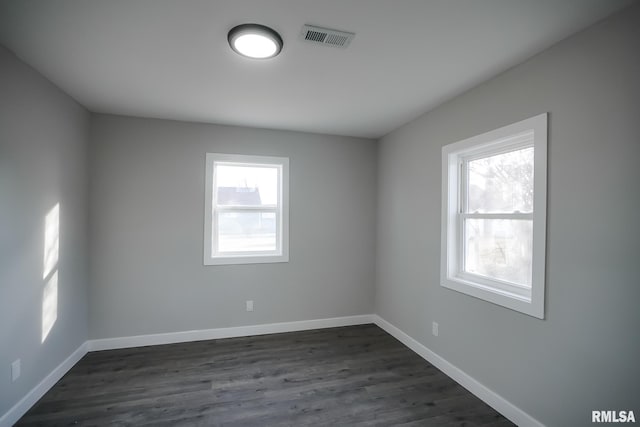 spare room with dark wood-style floors, a wealth of natural light, visible vents, and baseboards