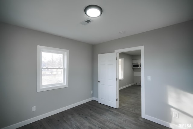 unfurnished bedroom featuring a walk in closet, dark wood finished floors, visible vents, and baseboards