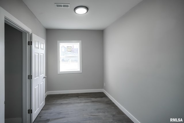 spare room with dark wood-type flooring, visible vents, and baseboards