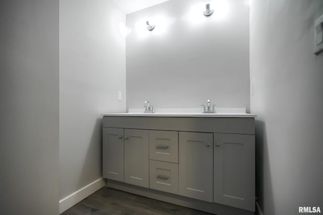 bathroom with double vanity, wood finished floors, a sink, and baseboards