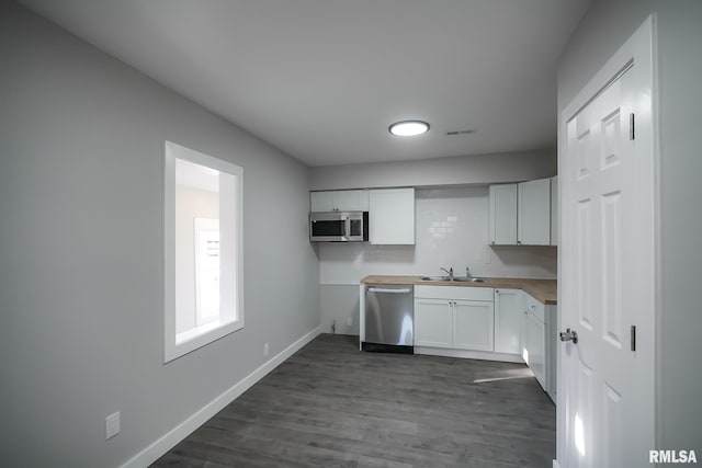 kitchen with stainless steel appliances, dark wood-type flooring, a sink, white cabinetry, and baseboards