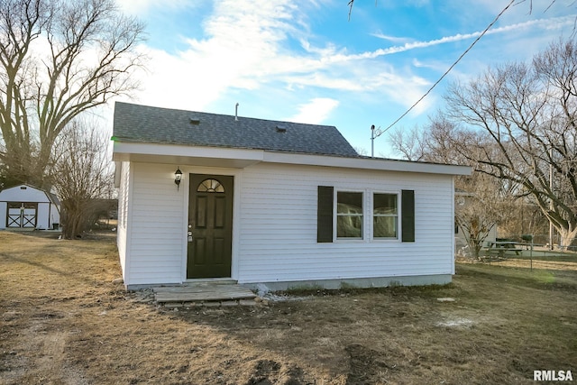 rear view of property featuring a yard, a shingled roof, an outdoor structure, and a detached garage