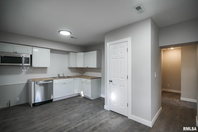 kitchen with dark wood finished floors, stainless steel appliances, visible vents, white cabinets, and a sink