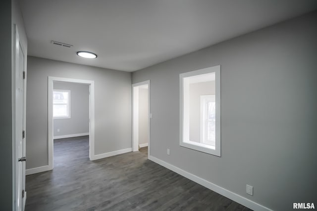 unfurnished room with dark wood-style floors, visible vents, and baseboards