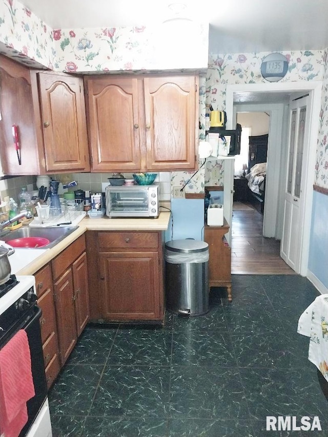 kitchen with wallpapered walls, a toaster, range, and a sink