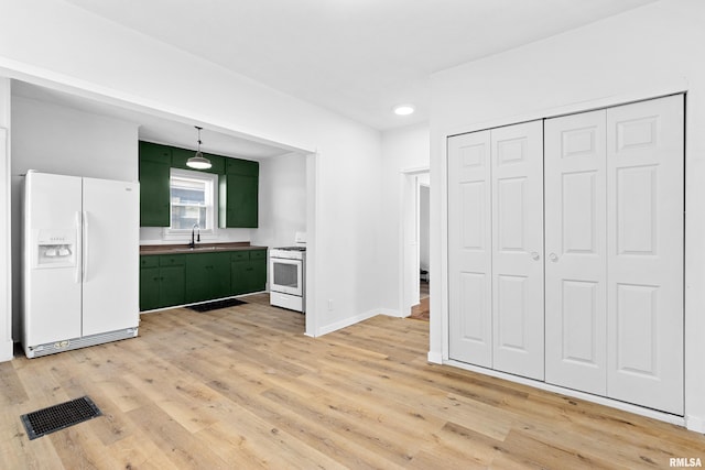 kitchen with white appliances, visible vents, light wood-style flooring, green cabinets, and a sink