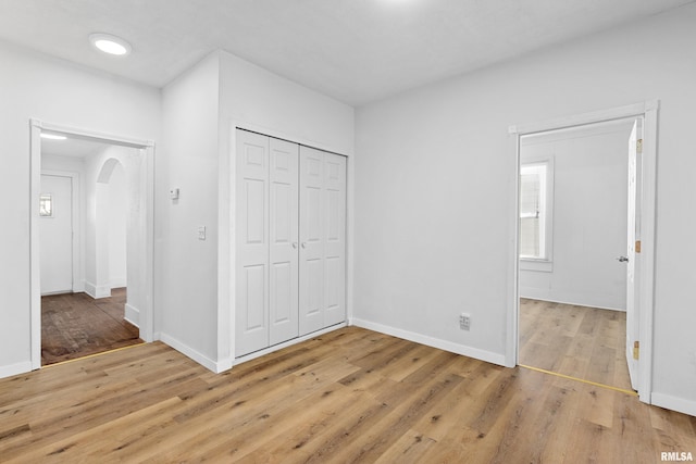 unfurnished bedroom with arched walkways, a closet, light wood-style flooring, and baseboards