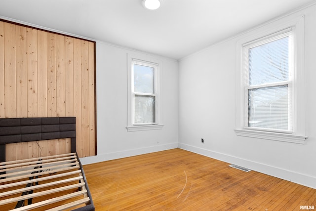 unfurnished bedroom featuring multiple windows, hardwood / wood-style flooring, visible vents, and baseboards