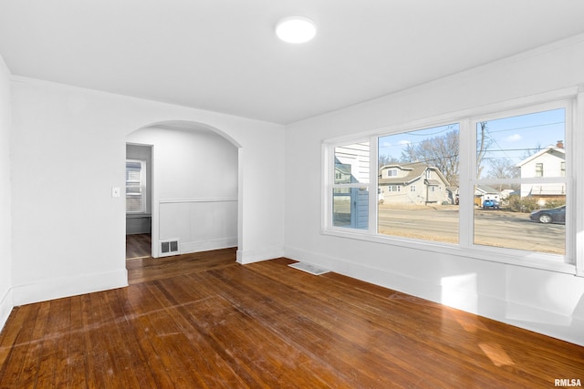 empty room featuring wood-type flooring, visible vents, arched walkways, and baseboards