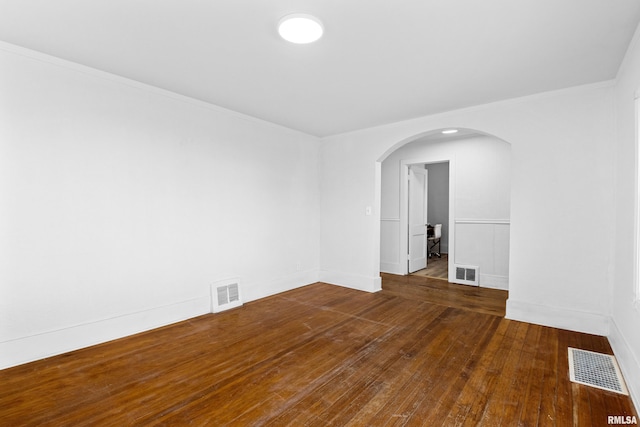 unfurnished room with hardwood / wood-style flooring, visible vents, and arched walkways