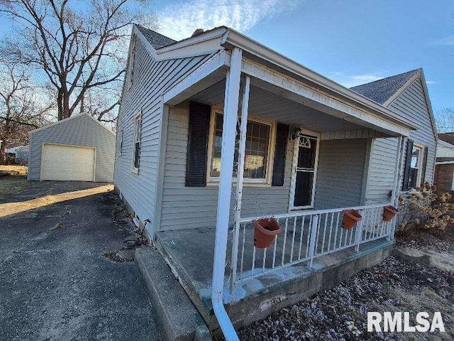 view of side of home featuring driveway, a porch, a detached garage, and an outdoor structure