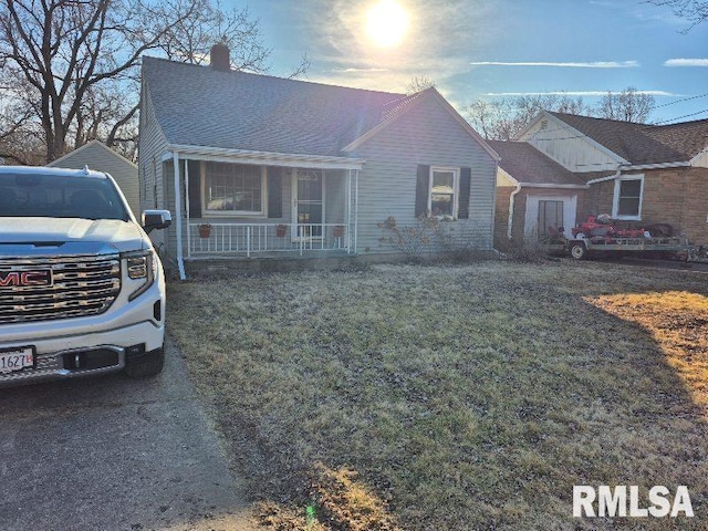 view of front of home featuring covered porch, roof with shingles, a front yard, and a chimney