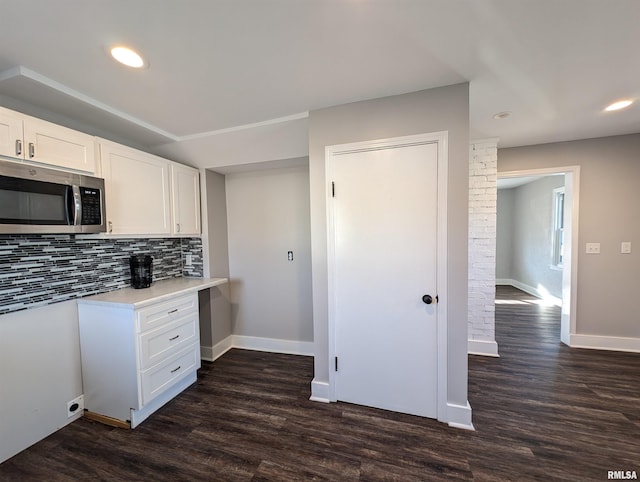 kitchen with dark wood-style flooring, stainless steel microwave, backsplash, and white cabinets